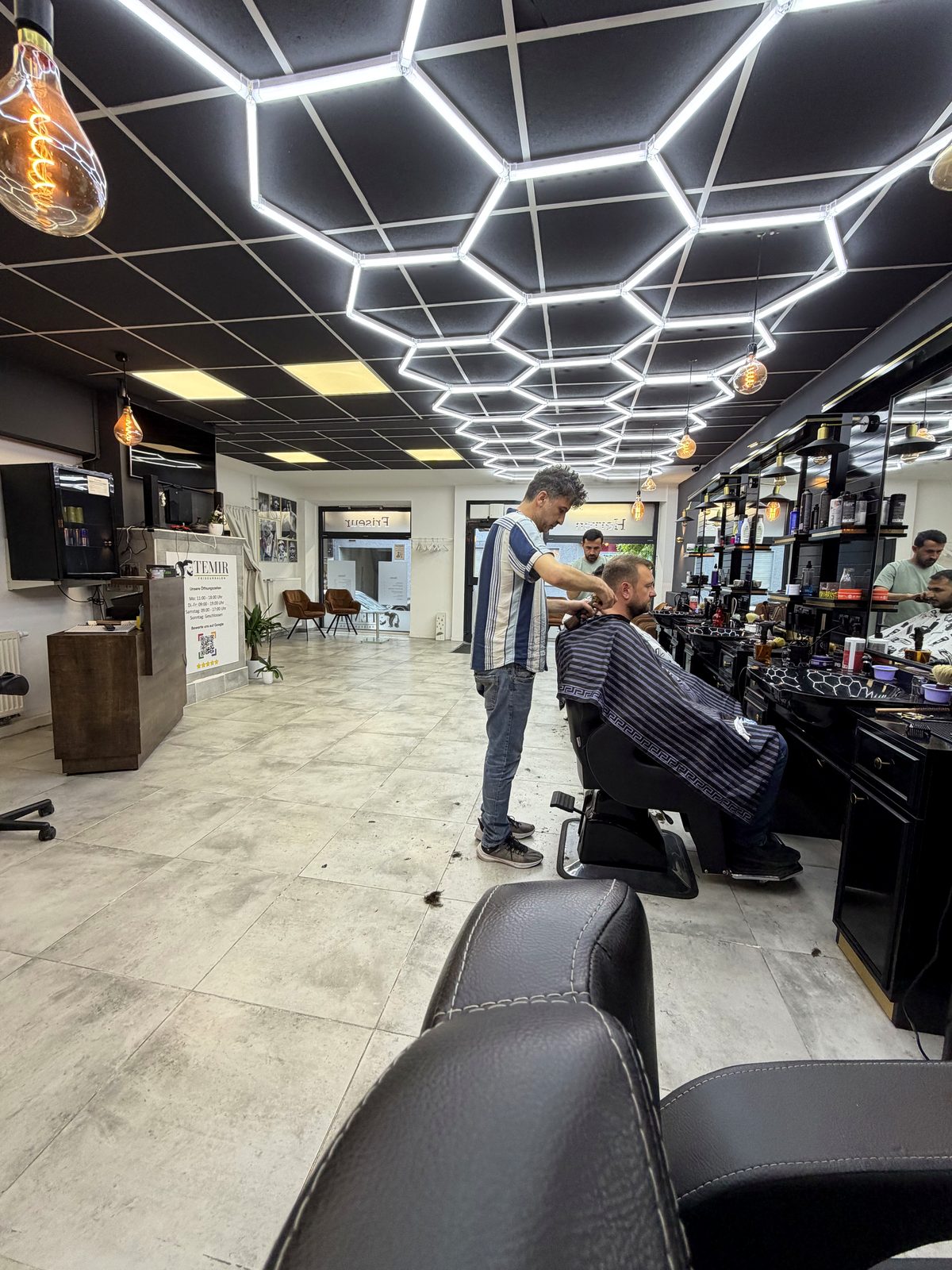 Barber bei der Arbeit unter der Hexagon-Beleuchtung im TEMIR Friseursalon Mühlacker